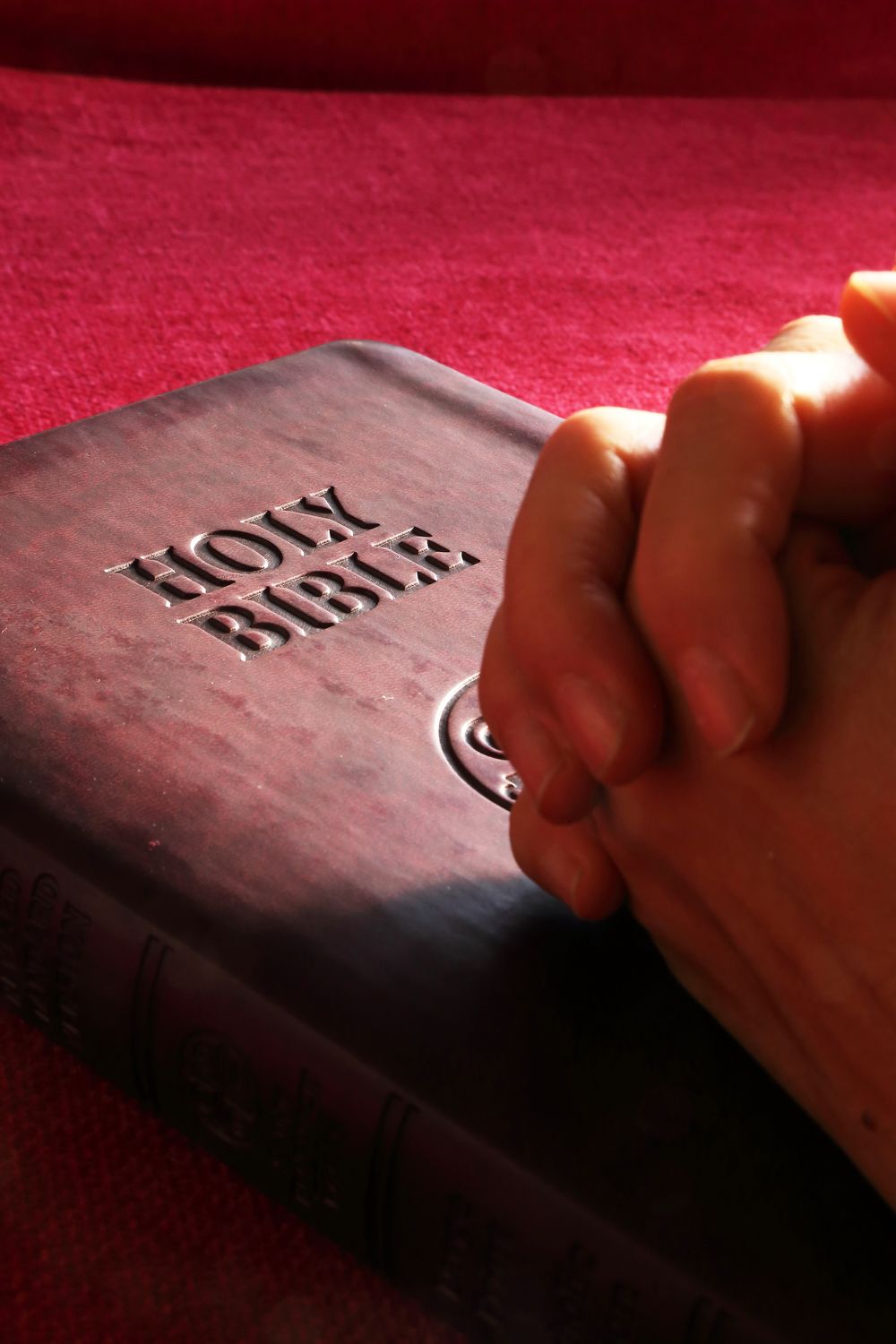 Hands folded in prayer beside a Bible